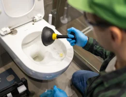 Un homme avec une ventouse à la main devant la cuvette des toilettes