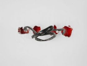A close-up of a tangled wire protruding from red holes in a white background.