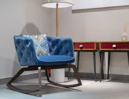 Comfortable blue armchair with cushion near lamp and wooden tables with diffusor in white room