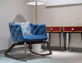 Comfortable blue armchair with cushion near lamp and wooden tables with diffusor in white room