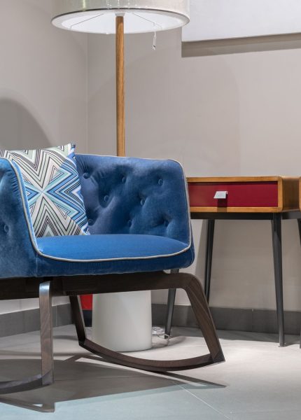 Comfortable blue armchair with cushion near lamp and wooden tables with diffusor in white room