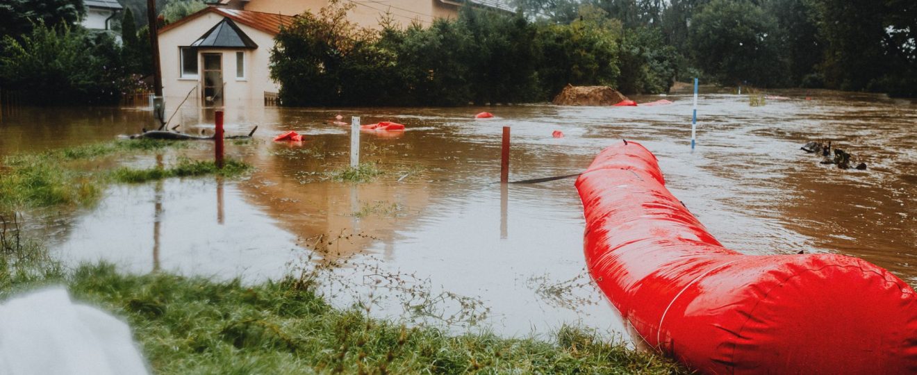 Flooded residential area protected by red flood barriers, showing severe weather impact.