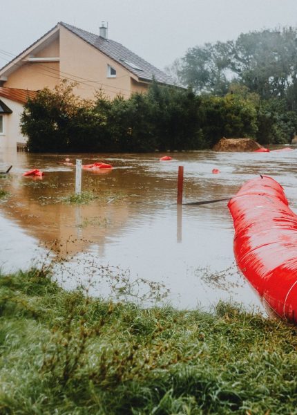 Flooded residential area protected by red flood barriers, showing severe weather impact.