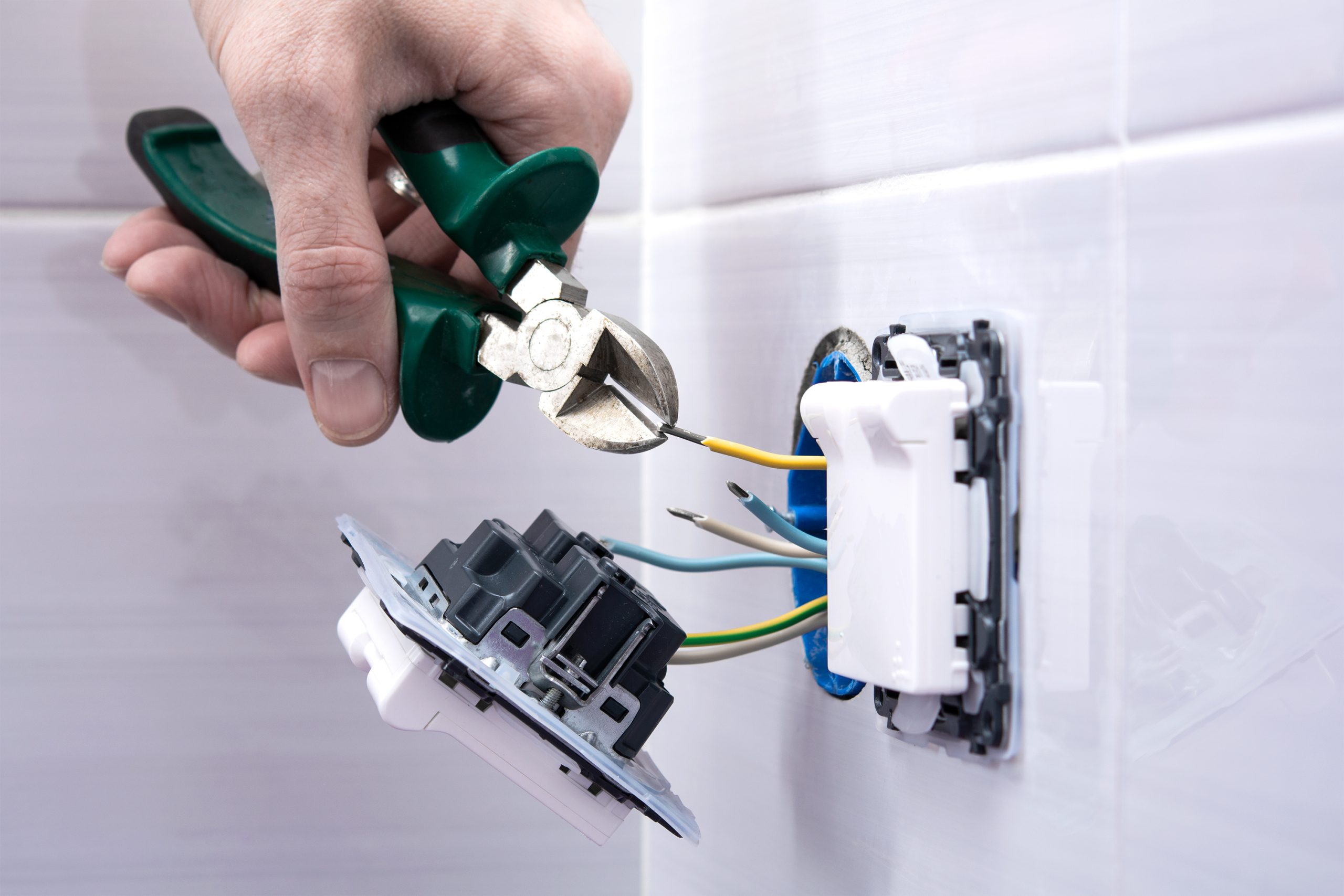 Electrician cutting wire with pliers in tiled wall