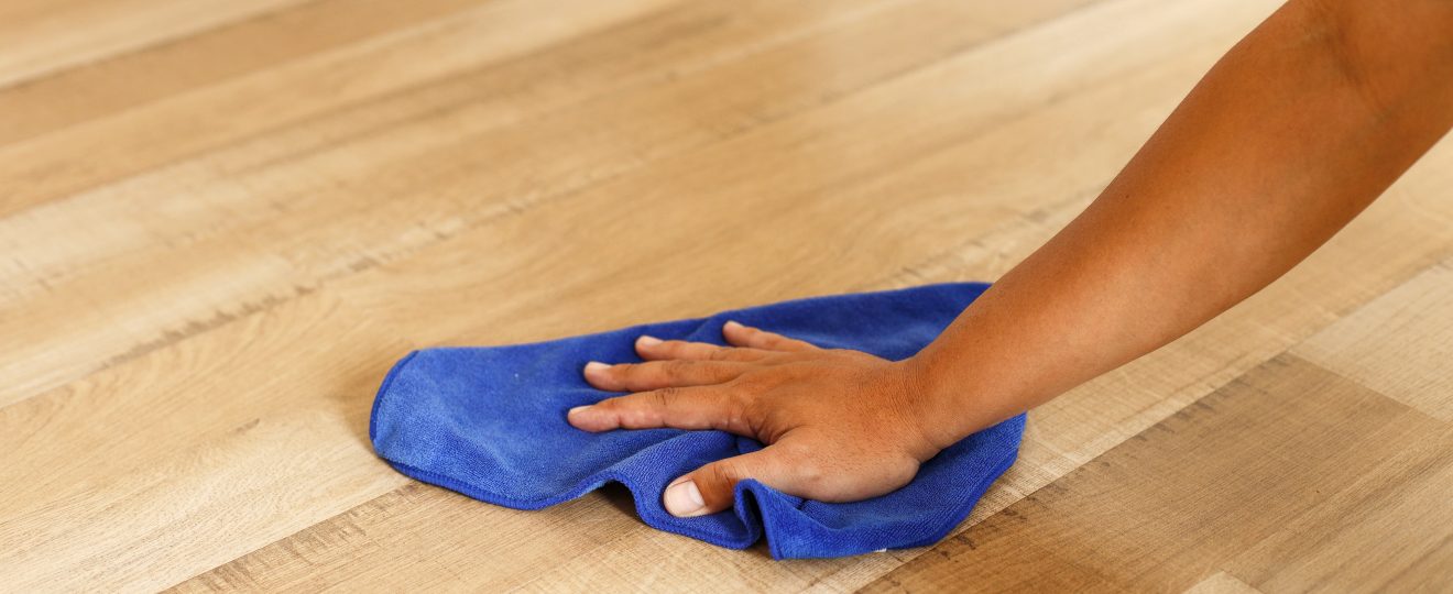 Hand cleaning wood floor with a blue rag
