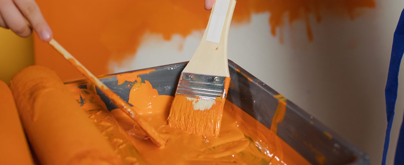 Hands applying bright orange paint to wall