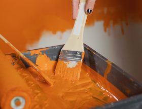 Hands applying bright orange paint to wall