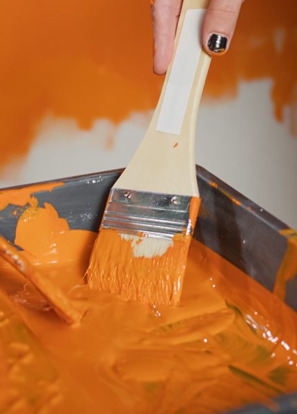 Hands applying bright orange paint to wall