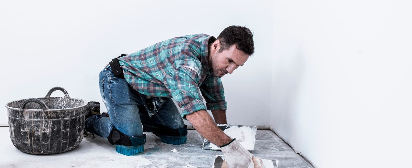 Man kneeling applying white compound to floor