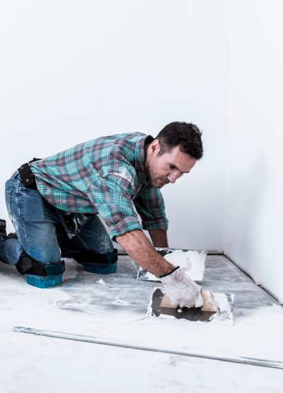 Man kneeling applying white compound to floor