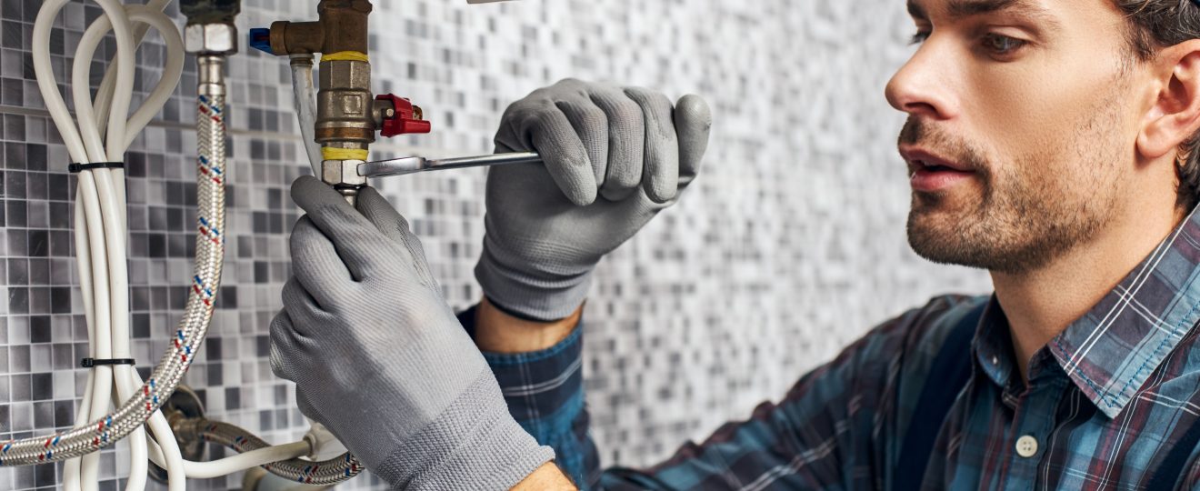 Plumber repairs pipe with wrench in home